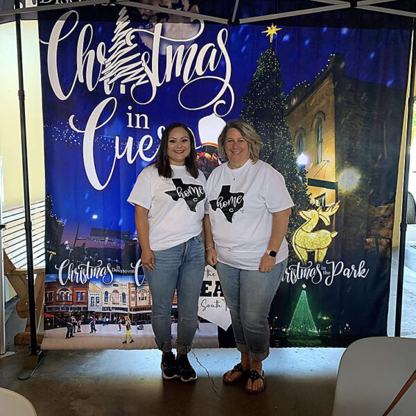 Texas State Fair 2022 - Day 2 - Photo of Samantha Bayfus (left) and Angie Cuellar in front of “Christmas in Cuero” booth backdrop